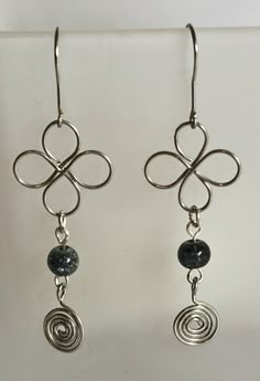 pair of silver earrings with black beads and wire work on them, hanging from hooks