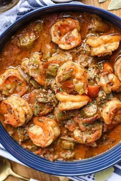 shrimp and vegetable stew in a blue bowl on a wooden table with silverware next to it