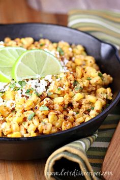 a skillet filled with mexican street corn and lime wedges