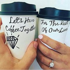 two people holding coffee mugs with writing on the cups and one is holding a diamond ring