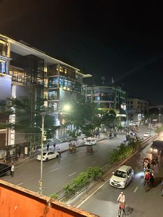 a busy city street at night with people riding bikes and cars driving down the road