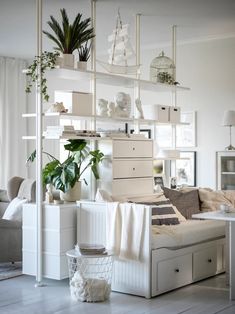 a living room filled with lots of white furniture and plants on top of shelving units