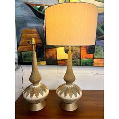 two lamps sitting on top of a wooden table next to a painting and lamp shade