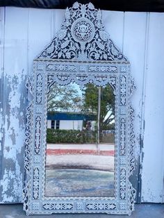 an ornate white mirror sitting on the side of a wall next to a building with a blue door