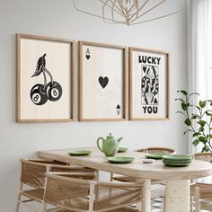 a dining room table with chairs and pictures on the wall above it, in front of a potted plant