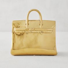 a shiny gold purse is sitting on a white surface, with the handle still attached to it