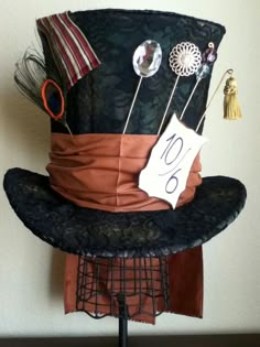 a top hat with pins and other items on it sitting on a metal stand in front of a white wall