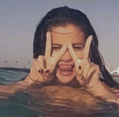 a woman holding her hands up to her face while floating in the water with two fingers on her face