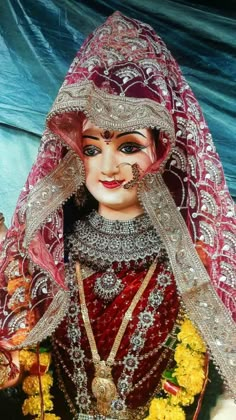 a statue of a woman in red and gold with flowers around her neck, wearing a veil