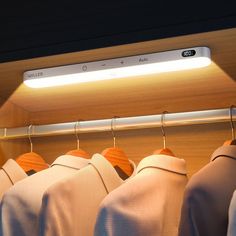 a row of shirts hanging on a rail in front of a closet with light coming from the ceiling