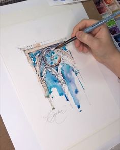 a person is holding a paintbrush and painting a picture with watercolors on paper