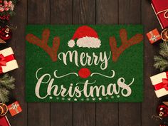 a merry christmas door mat surrounded by presents on a wooden table with red and green bows