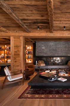 the living room is decorated in rustic wood and features a fireplace, two chairs, an ottoman, and several bookshelves