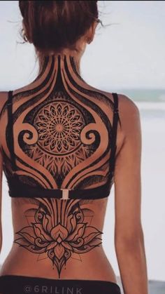 a woman with tattoos on her back standing in front of the ocean