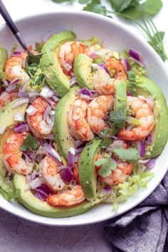 a salad with shrimp, avocado and cilantro in a white bowl