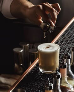 a person pours coffee into a glass on top of a table with liquor bottles