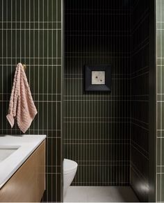 a bathroom with green tiled walls and white counter tops, along with a pink towel hanging on the wall