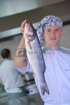 a man in chef's hat holding up a fish on a plate and smiling