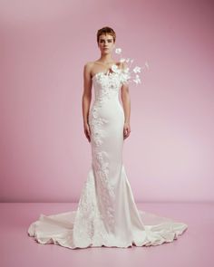 a woman in a white wedding dress with flowers on her head and shoulders, standing against a pink background