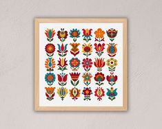 a cross stitch pattern with colorful flowers on white paper in a wooden frame hanging on a wall