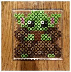 a square shaped object made out of beads on a wooden table with a wood floor