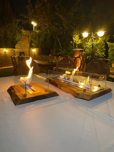 two fire pits sitting on top of a table covered in white cloth and lit candles