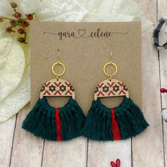 a pair of earrings with tassels on top of a wooden table next to a card