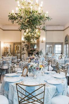 a room filled with tables and chairs covered in blue table cloths next to a chandelier