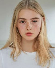 a young woman with freckles on her face looking at the camera while wearing a white t - shirt