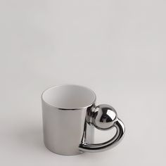 a stainless steel cup with a handle on a white surface, in the shape of a heart