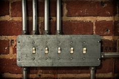 an electrical device mounted to a brick wall with metal pipes and wires attached to it