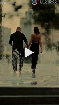 a man and woman walking down a street holding hands in front of a water fountain