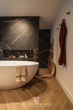 a bath tub sitting next to a wooden floor in a bathroom with marble walls and floors