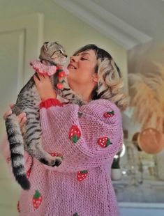 a woman holding a cat in her arms and kissing it's face while wearing a pink sweater