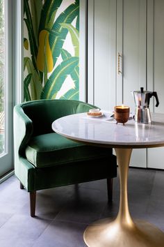 a green chair sitting next to a table with a coffee pot on top of it