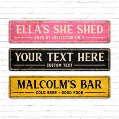 three different colored street signs on a white brick wall with the words, ella's she shed, your text here and malcolm's bar