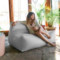 a woman sitting on a bean bag chair in the living room with potted plants