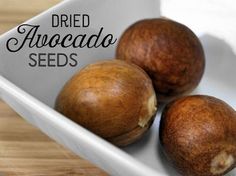 three avocados in a white bowl on a wooden table with the words dried avocado seeds