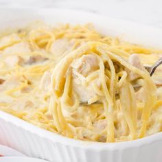 a spoon full of chicken alfredo in a white casserole dish