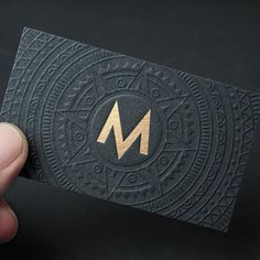 a hand holding up a business card with the letter m on it's side