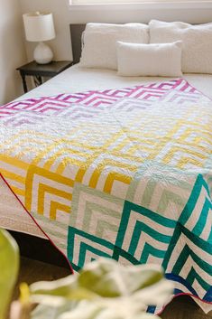 a bed with a colorful quilt on it next to a potted plant in front of a window