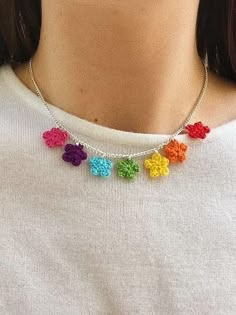 a woman wearing a multicolored crochet necklace with flowers on it's chain