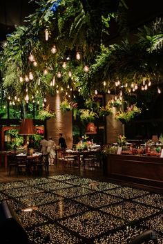 the restaurant is decorated with greenery and hanging lights above the dining area, while people are seated at tables