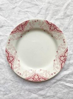 a red and white plate sitting on top of a white tablecloth covered floor next to a cup