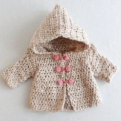 a crocheted jacket with pink buttons on the front and hood is laying on a white surface