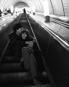 a man and woman sitting on an escalator in a subway station, looking at each other