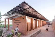 a man walking past a brick building with a metal roof over it's entrance