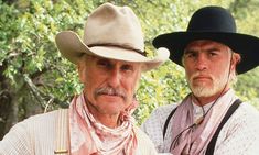 two men in cowboy hats and scarves pose for a photo together with trees in the background