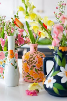 three vases with flowers painted on them sitting on a white table next to each other