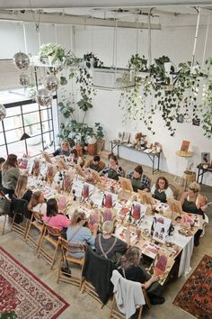 a group of people sitting at tables in a room with plants hanging from the ceiling